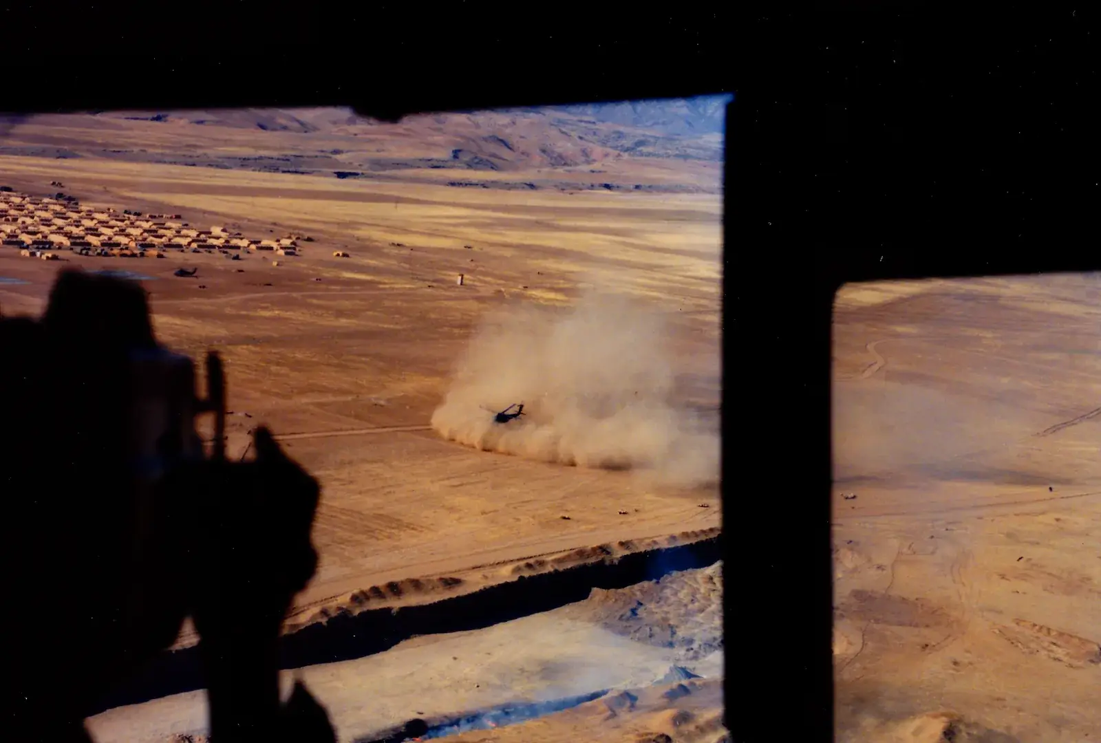 A helicopter landing in a cloud of desert dust, photographed from the door of another aircraft